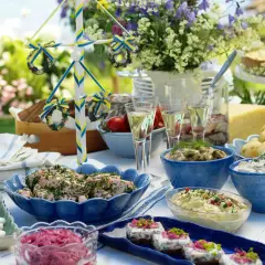 En dukning med typisk svensk midsommarmat: sill, ägg, potatis, paj och en midsommarstång.