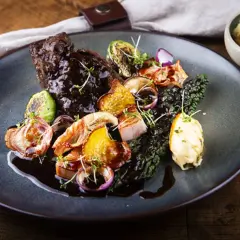 En tallrik med mustig oxkind, rostade rotfrukter, grönkål och en klick örtsmör. Ett perfekt oxkind recept för en festmåltid.