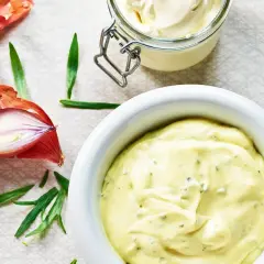 En skål med krämig falsk bearnaisesås kall, bredvid schalottenlök och en visp med sås.