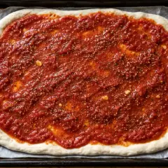 En pizzabotten täckt med en smakrik tomatsås, perfekt för ditt tomatsås recept. Kryddor och vitlök syns i såsen.