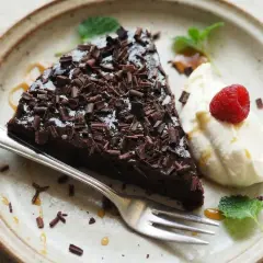 En bit kladdkaka med chokladtopping och hallon, serverad med grädde. Perfekt för dig som vill ha glutenfria kladdkakemuffins.