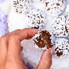 En hand håller en bit av en chokladboll, täckt av vita pärlsocker. Ett enkelt chokladbollar recept för fika.