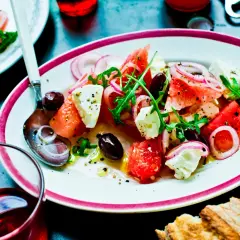 En uppfriskande melon och fetaostsallad med oliver, rödlök och ruccola, serverad på en tallrik med en sked.