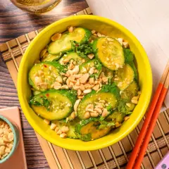 En skål med asiatisk gurksallad, toppad med hackade jordnötter och färska örter. Serveras med ätpinnar.