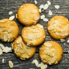 Sju gyllene bondkakor med mandelflagor på en mörk träyta. Perfekt för ditt bondkakor recept.