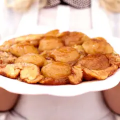 En gyllene tarte tatin med karamelliserade äpplen på en vit tallrik, redo att serveras.