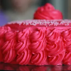 En vacker rosa tårta med rosettmönster i frosting och små vita strössel. Perfekt för ett firande!
