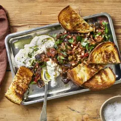 En krämig, vegetarisk midsommarmat med rostade grönsaker, oliver, pinjenötter och vitlöksbröd på ett serveringsfat.