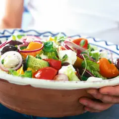 En stor skål med en god sallad till maten, full av färska grönsaker som tomat, gurka, paprika, lök och fetaost.