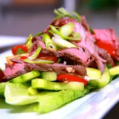 En läcker asiatisk biffsallad med tunt skivad biff, gurka, tomat och salladslök på en bädd av krispig sallad.