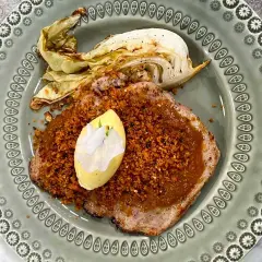 Schnitzel med krispigt täcke och en klick kall sås, garnerad med en blomma. Serveras med ugnsrostad kål.