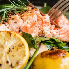 En saftig bit lax i ugn, kryddad med peppar och rosmarin, serverad med citron, körsbärstomater och gröna blad.