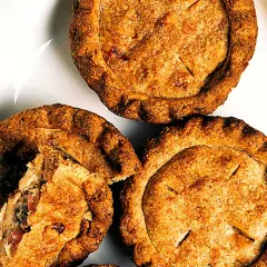 Tre gyllene små pajer på en vit tallrik. En paj är uppskuren och visar ett smakrikt innehåll. Perfekt för en fika!