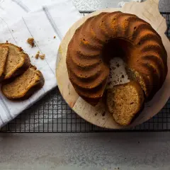 En saftig mjuk pepparkaka med en skiva uppskuren, serverad på en träskärbräda. Tre skivor ligger på en randig duk.