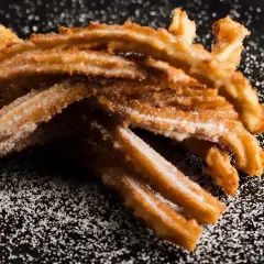 Krispiga churros, pudrade med socker, redo att avnjutas. Ett enkelt churros recept för hemmabruk.