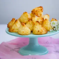 En hög med gyllene kokostoppar på ett turkost fat, redo att avnjutas. Ett enkelt kokostoppar recept som ger ljuvliga små bakverk.