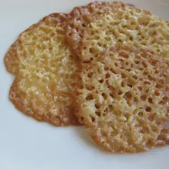 Tre gyllene havreflarn utan sirap ligger på en vit tallrik. De är tunna och krispiga med ett vackert mönster av små hål.