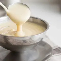 Krämig vaniljsås hälls upp ur en slev i en skål. Perfekt för ditt vaniljsås recept!