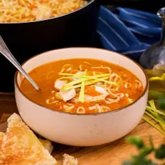 En skål med kycklingsoppa med nudlar och grönsaker, perfekt för ett enkelt kycklingsoppa recept. Serveras med rostat bröd och en flaska olivolja.