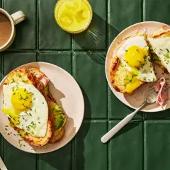 Två läckra croque madame med stekt ägg och avokado, serverade med kaffe och juice.