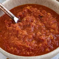 En skål med hemgjord chilisås, perfekt för ditt nästa chilisås recept. En sked i skålen visar den rika, kryddiga konsistensen.