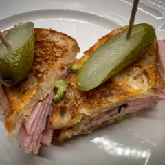 A halved Reuben sandwich with pickles on toothpicks, served on a white plate.