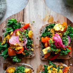 Fyra goda mackor med tofu scramble, grönkål, paprika och rödlök på grovt bröd, serverade på en träskärbräda.
