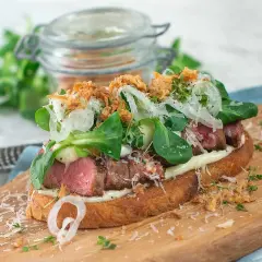En läcker steak sandwich med saftigt kött, krispig sallad, hyvlad parmesan och friterad lök på rostat bröd.