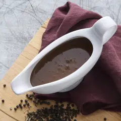 En vit såssip med mustig brunsås, omgiven av pepparkorn och en vinröd duk. Perfekt för ditt brunsås recept.