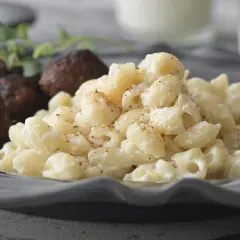 En tallrik med stuvade makaroner och köttbullar, garnerad med en kvist örter. En klassisk svensk husmanskosträtt.