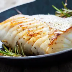 En saftig bit kokt torsk med gyllene, krispig yta, serverad med rosmarin i en mörk panna.