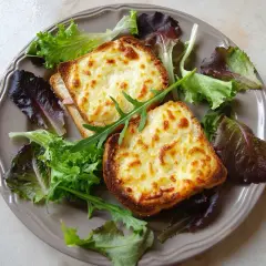 Två gyllene croque monsieur med smält ost och en fräsch sallad på en tallrik.