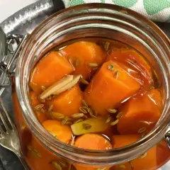 En glasburk med bitar av picklad morot, fänkålsfrön och vitlök. En gaffel ligger bredvid.