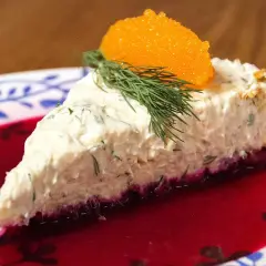 En bit lax cheesecake med dill och rom på en tallrik med rödbetsjuice.