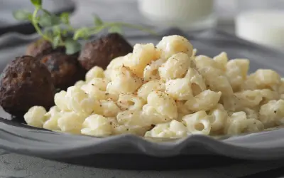 En tallrik med stuvade makaroner och köttbullar, garnerad med en kvist örter. En klassisk svensk husmanskosträtt.