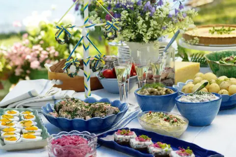 En dukning med typisk svensk midsommarmat: sill, ägg, potatis, paj och en midsommarstång.