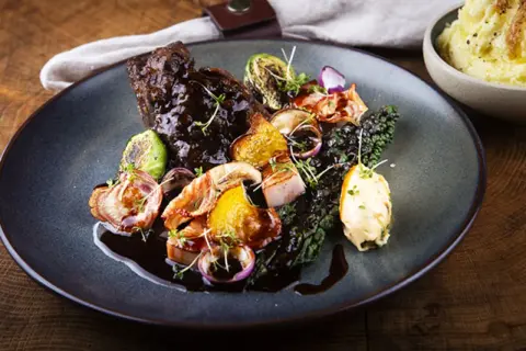 En tallrik med mustig oxkind, rostade rotfrukter, grönkål och en klick örtsmör. Ett perfekt oxkind recept för en festmåltid.