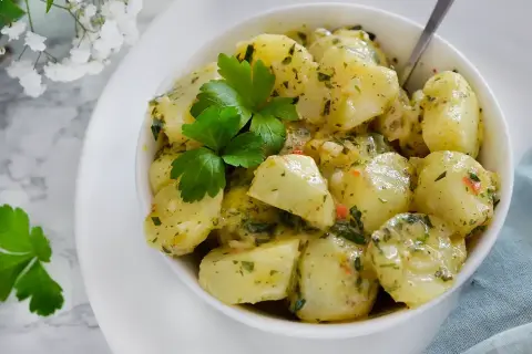 En skål med ljummen potatissallad, toppad med färsk persilja. Perfekt till grillat eller som en lätt lunch.