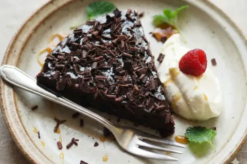 En bit kladdkaka med chokladtopping och hallon, serverad med grädde. Perfekt för dig som vill ha glutenfria kladdkakemuffins.