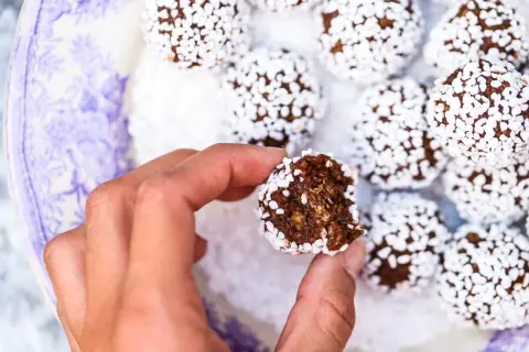 En hand håller en bit av en chokladboll, täckt av vita pärlsocker. Ett enkelt chokladbollar recept för fika.