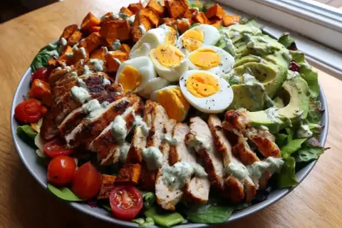 Enkel sallad med grillad kyckling, kokta ägg, sötpotatis, avokado och körsbärstomater, toppad med en krämig dressing.