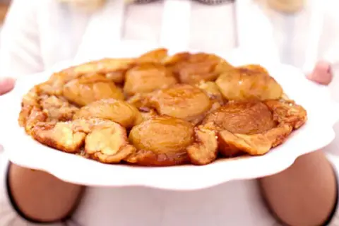 En gyllene tarte tatin med karamelliserade äpplen på en vit tallrik, redo att serveras.