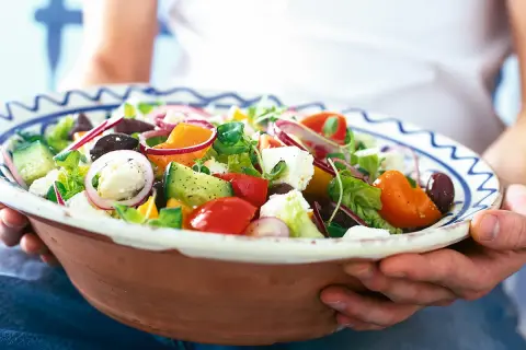 En stor skål med en god sallad till maten, full av färska grönsaker som tomat, gurka, paprika, lök och fetaost.