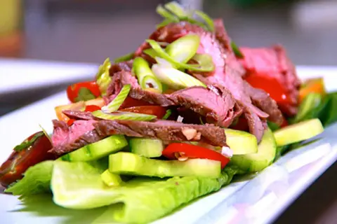 En läcker asiatisk biffsallad med tunt skivad biff, gurka, tomat och salladslök på en bädd av krispig sallad.