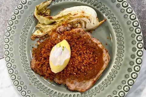 Schnitzel med krispigt täcke och en klick kall sås, garnerad med en blomma. Serveras med ugnsrostad kål.