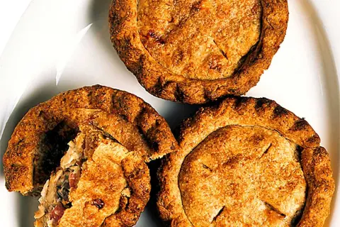 Tre gyllene små pajer på en vit tallrik. En paj är uppskuren och visar ett smakrikt innehåll. Perfekt för en fika!
