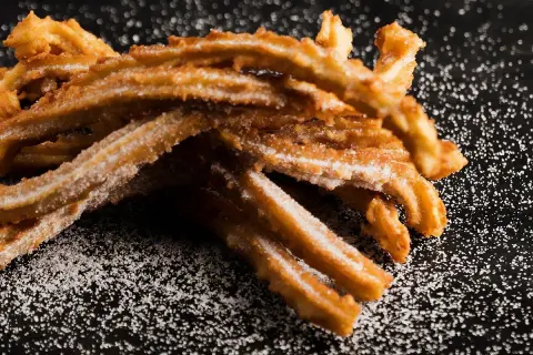 Krispiga churros, pudrade med socker, redo att avnjutas. Ett enkelt churros recept för hemmabruk.