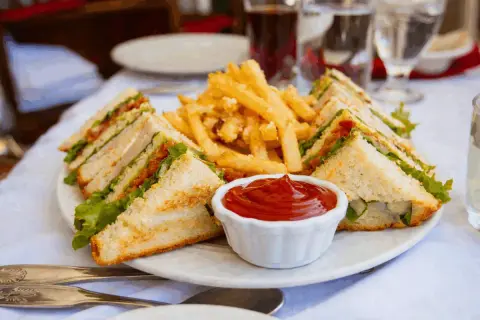 En tallrik med en klassisk club sandwich, pommes frites och ketchup. Perfekt för en lunch!