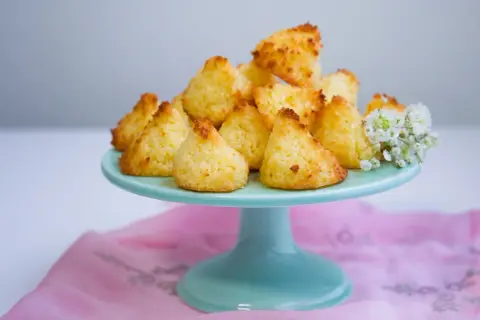 En hög med gyllene kokostoppar på ett turkost fat, redo att avnjutas. Ett enkelt kokostoppar recept som ger ljuvliga små bakverk.