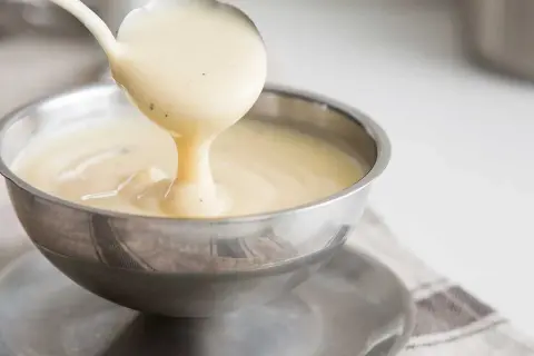 Krämig vaniljsås hälls upp ur en slev i en skål. Perfekt för ditt vaniljsås recept!